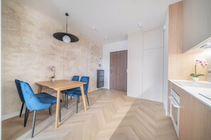 A modern kitchen with white cabinets, a wooden herringbone floor, and a dining area with blue chairs and a wooden table. - Kierbedzia Suite (Warszawa)