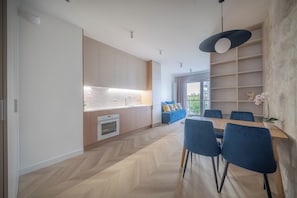 A modern kitchen with built-in appliances, a dining area with blue chairs, and a large window. - Kierbedzia Suite (Warszawa)
