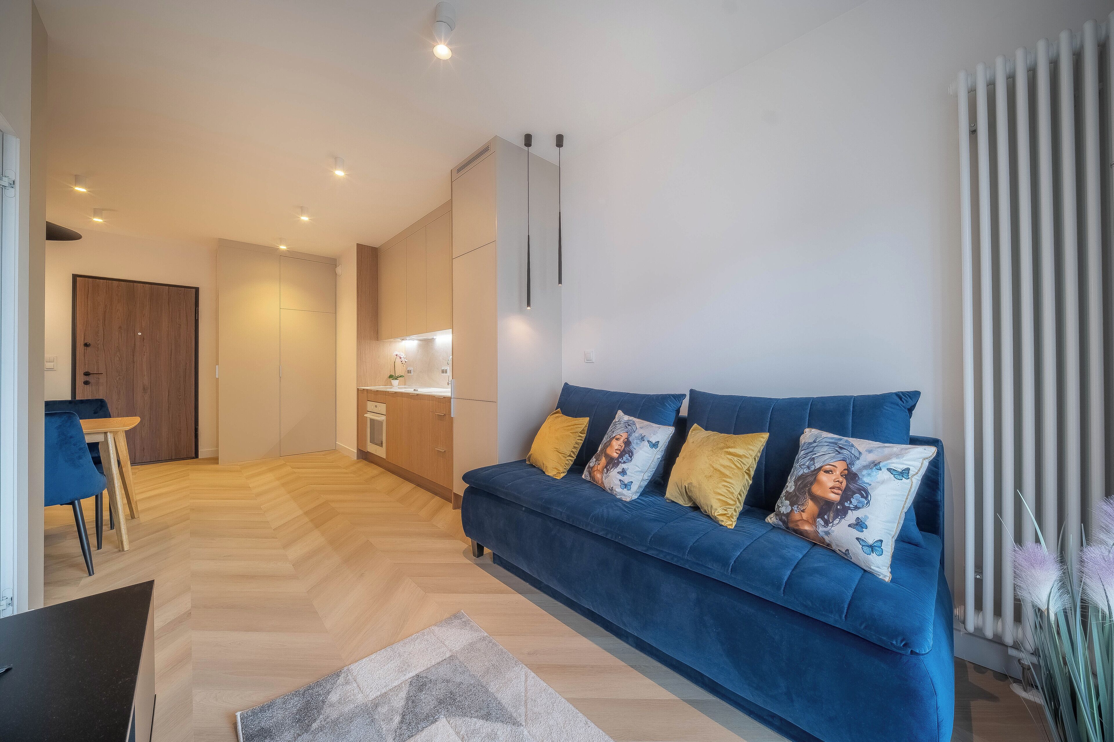 Una sala moderna con un sofá azul, suelo de madera y una cocina al fondo.