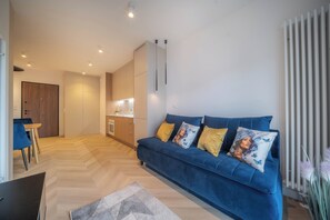 Un salon moderne avec un canapé bleu, un plancher en bois et une cuisine en arrière-plan.