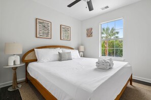 A bedroom with a bed, two wall-mounted lamps, a ceiling fan, and a window with a view of palm trees. - The Chantrell Pool Hot Tub Pets (North Charleston)
