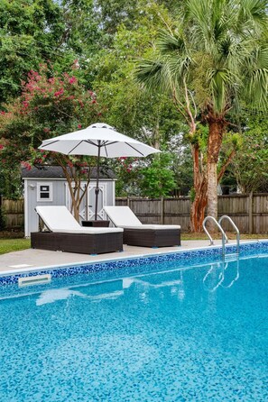 A swimming pool with a tiled edge, a lounge area with two chairs and a table, and a palm tree in the background. - The Chantrell Pool Hot Tub Pets (North Charleston)
