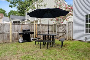 An outdoor patio with a grill, table, chairs, and an umbrella. - The Chantrell Pool Hot Tub Pets (North Charleston)