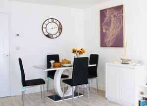 Uma sala de jantar com mesa redonda, cadeiras pretas, um relógio e um quadro na parede.