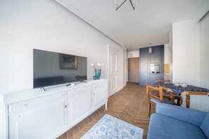 Una sala de estar moderna con un televisor de pantalla plana, un mueble blanco, un sofá azul y un tapete estampado.