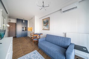 A modern living room with a blue sofa, wooden dining table, and a kitchen in the background. - Kierbedzia Elegant Classic Blinds, Free Parking, Mokotow, Warsaw (Warszawa)