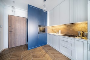 A modern kitchen with blue cabinets, a wooden door, and a herringbone-patterned floor. - Kierbedzia Elegant Classic Blinds, Free Parking, Mokotow, Warsaw (Warszawa)