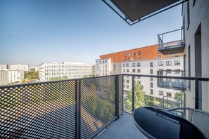Un balcón con vista a edificios circundantes, una mesa de vidrio y una baranda de metal.