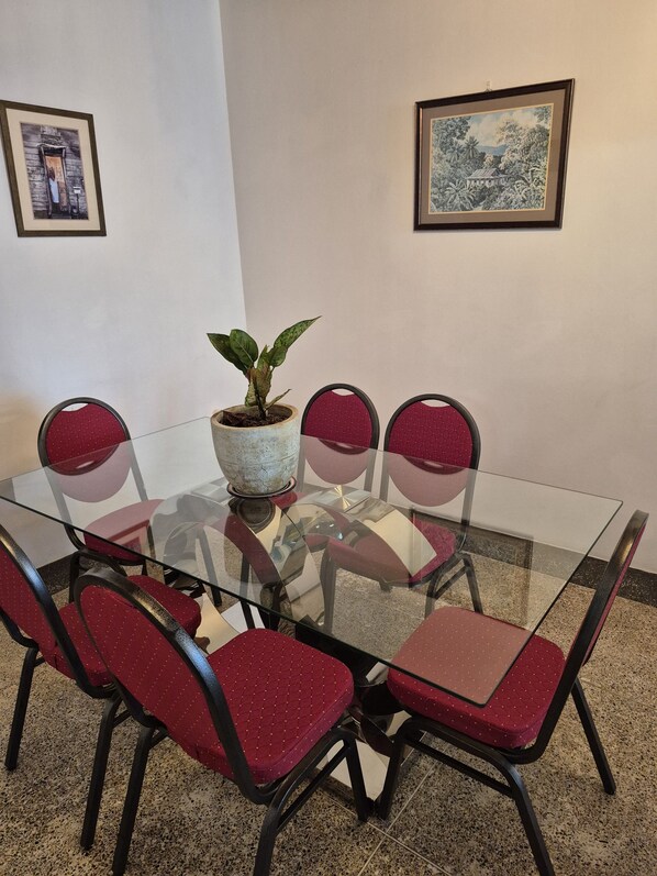 A glass-top table with six red chairs, a potted plant, and two framed pictures on the wall.