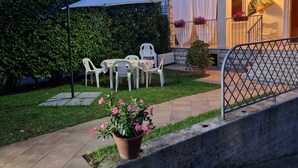 An outdoor patio with a table and chairs, a potted plant, and a covered area with a chair. - CasaMiria: a cozy apartment just 5 minutes from Forte dei Marmi, with a garden (Seravezza)