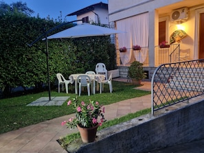 An outdoor patio with a table and chairs, a potted plant, and a covered area with a chair.