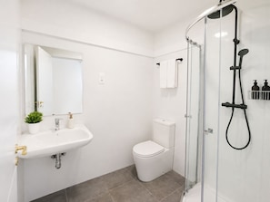 Un baño moderno con ducha de vidrio, lavamanos blanco con grifo dorado y un inodoro.