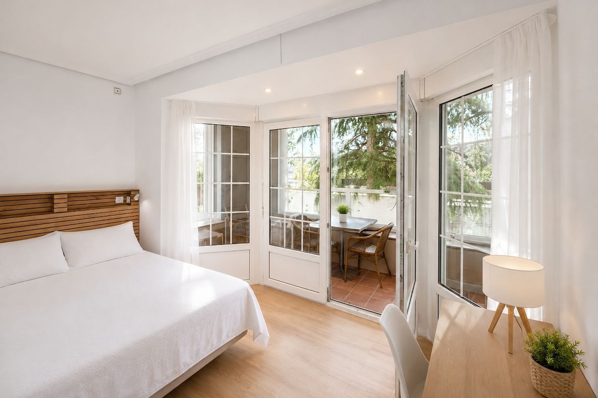 A bedroom with a bed, a dining area with a table and chairs, and a sliding glass door leading to an outdoor patio.