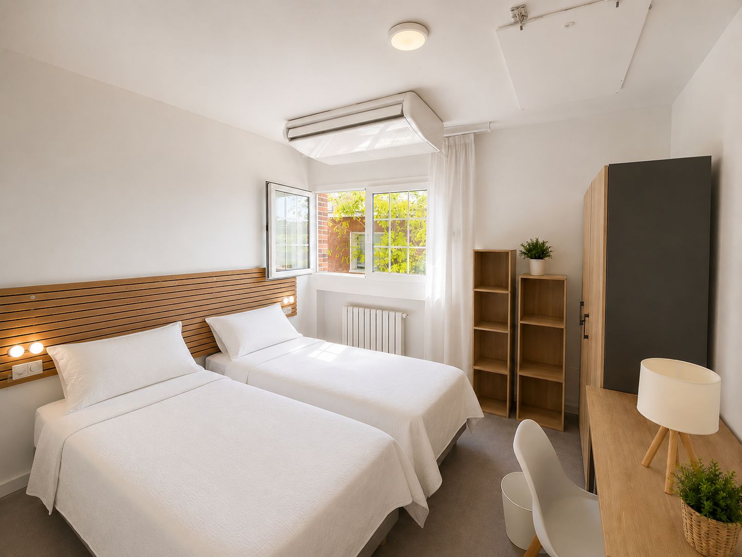 A hotel room with two beds, a desk, a chair, a wardrobe, and a window with a view of greenery.