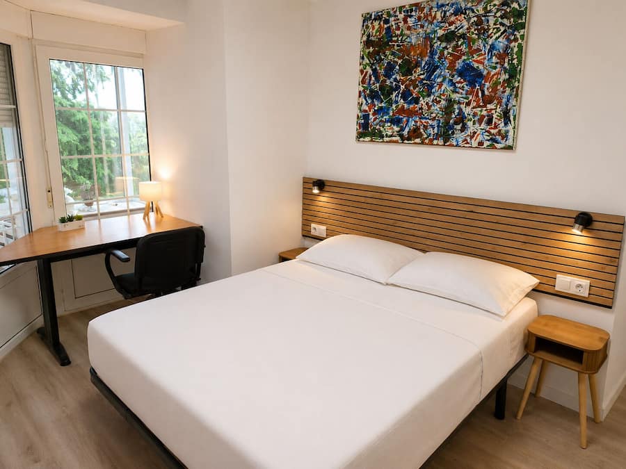 Un dormitorio con cama, mesitas de noche, escritorio y ventana.
