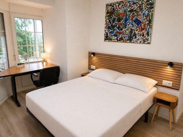 A bedroom with a bed, bedside tables, a desk, and a window.