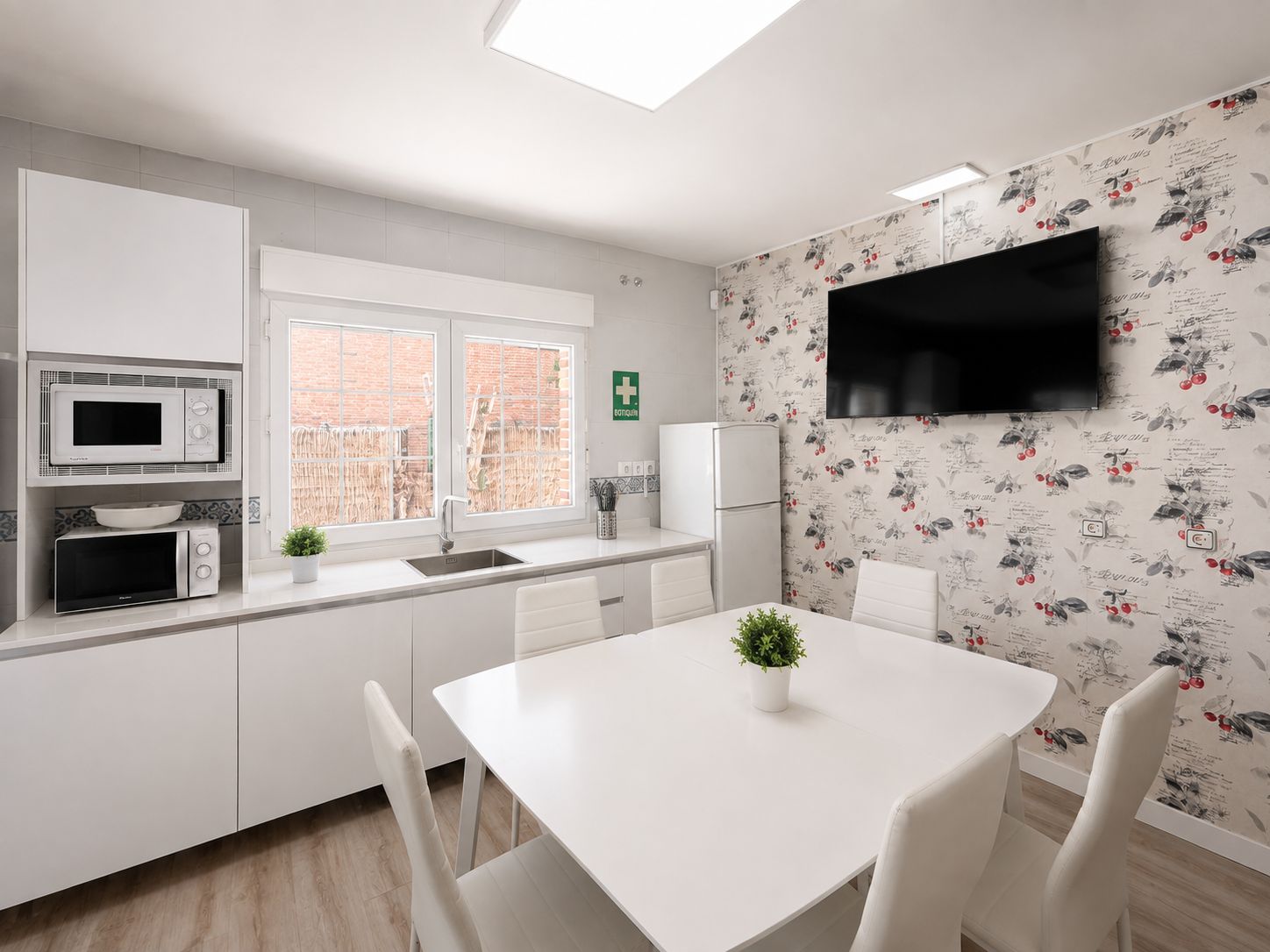 Una cocina moderna con armarios blancos, microondas, refrigerador y un comedor con mesa y sillas blancas.