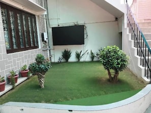 A courtyard with artificial grass, potted plants, and a staircase. - Swaraj Homestay (Varanasi)