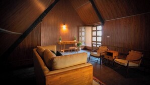 Een gezellige kamer met schuine wanden, houten lambrisering, een bank, stoelen, een tafeltje en een raam met uitzicht.