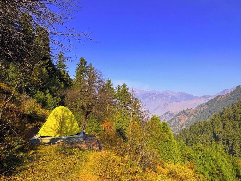 Une tente installée sur un promontoire rocheux, avec une chaîne de montagnes en arrière-plan.