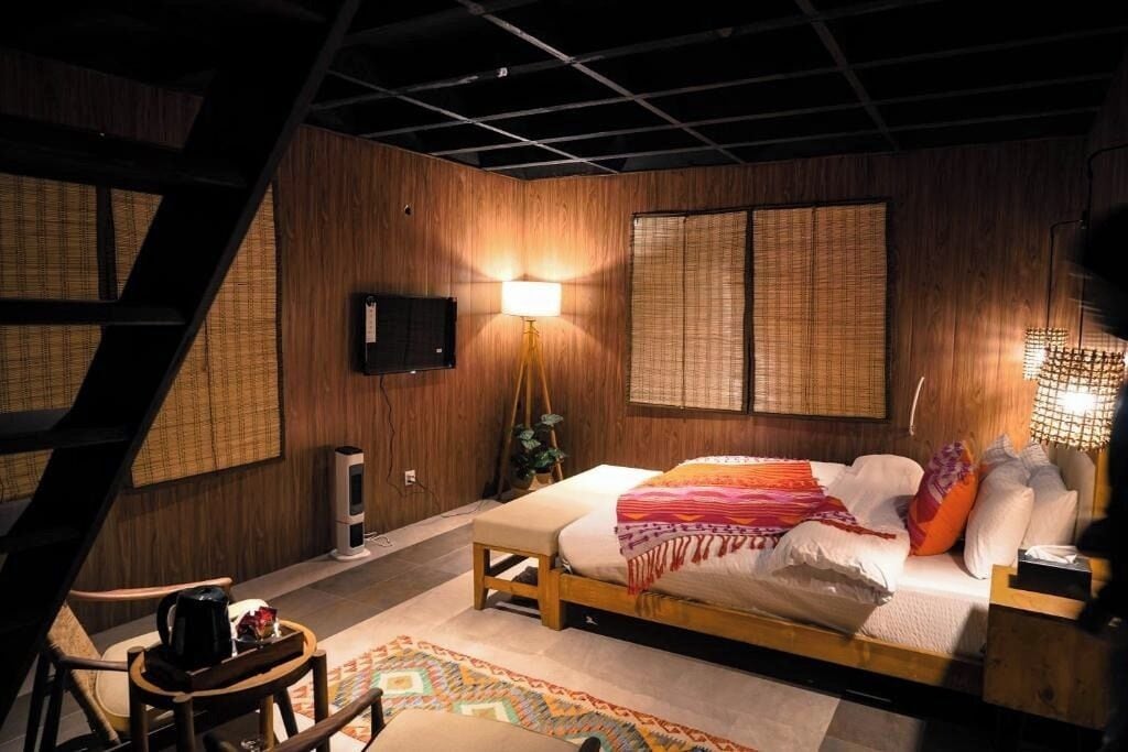 Quarto com cama, luminária de cabeceira e televisão na parede.