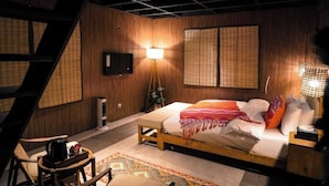 Een slaapkamer met een bed, nachtlampjes, een televisie en een raam met bamboeblinden.