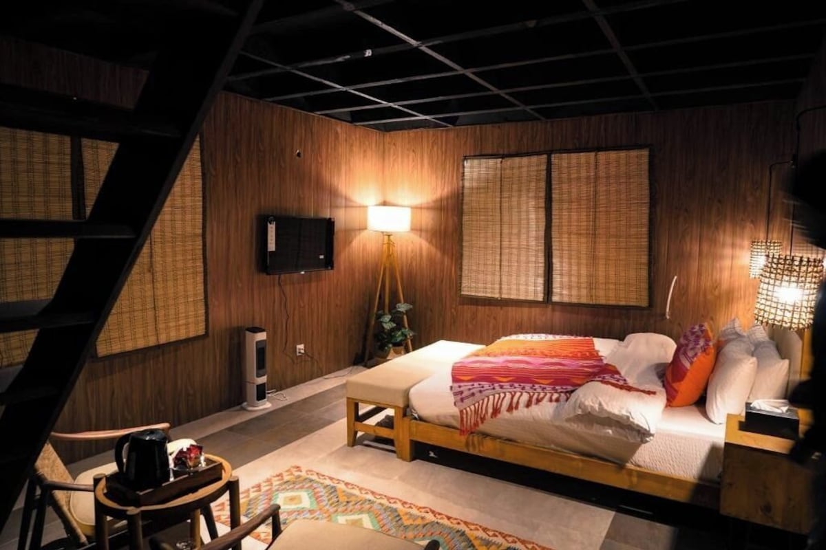 Une chambre à coucher avec un lit, des lampes de chevet, un téléviseur et une fenêtre avec des stores en bambou.