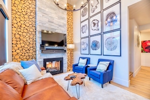 A modern living room with a fireplace, blue sofas, and a stone wall with a log pattern. - Upstay Lake Dillon Basecamp Mountain Trails (Silverthorne)