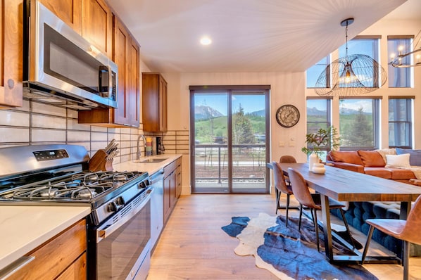 A modern kitchen with a built-in microwave, stove, and oven. There is a dining area with a wooden table and chairs. - Upstay Lake Dillon Basecamp Mountain Trails (Silverthorne)