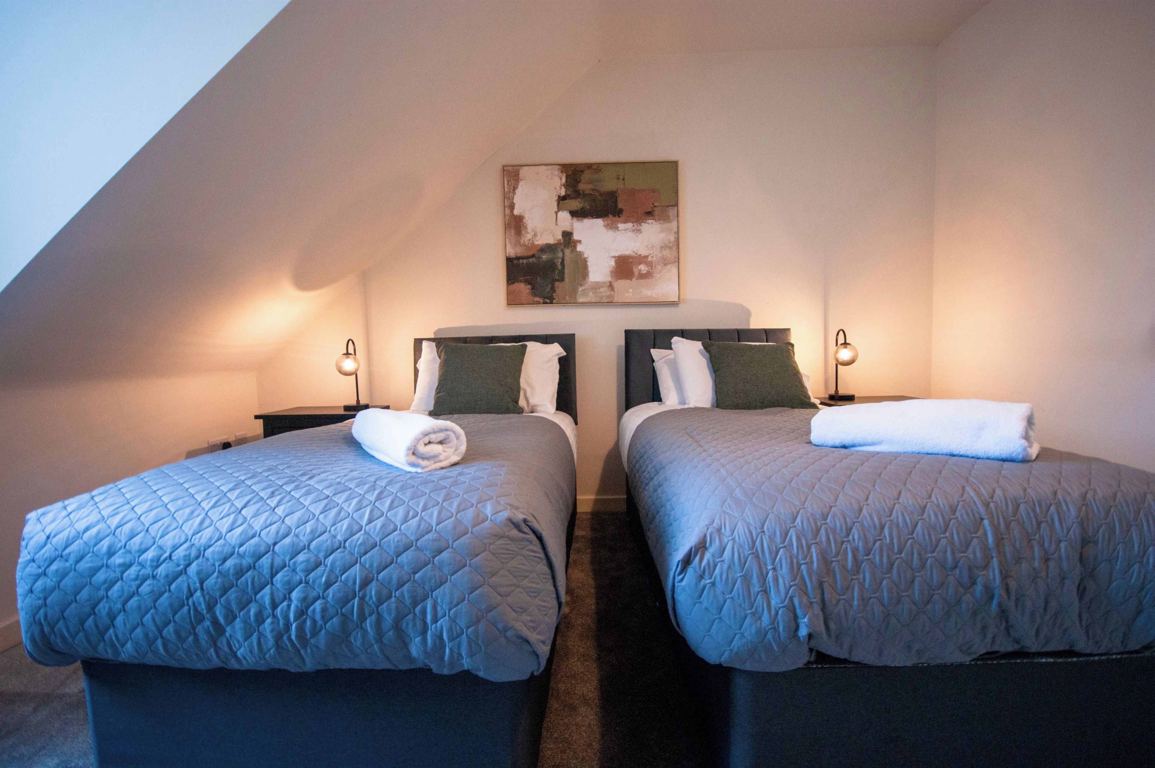 Ein Zimmer mit zwei Betten, jeweils mit Kopfteil, einem Bild an der Wand und Nachttischlampen.