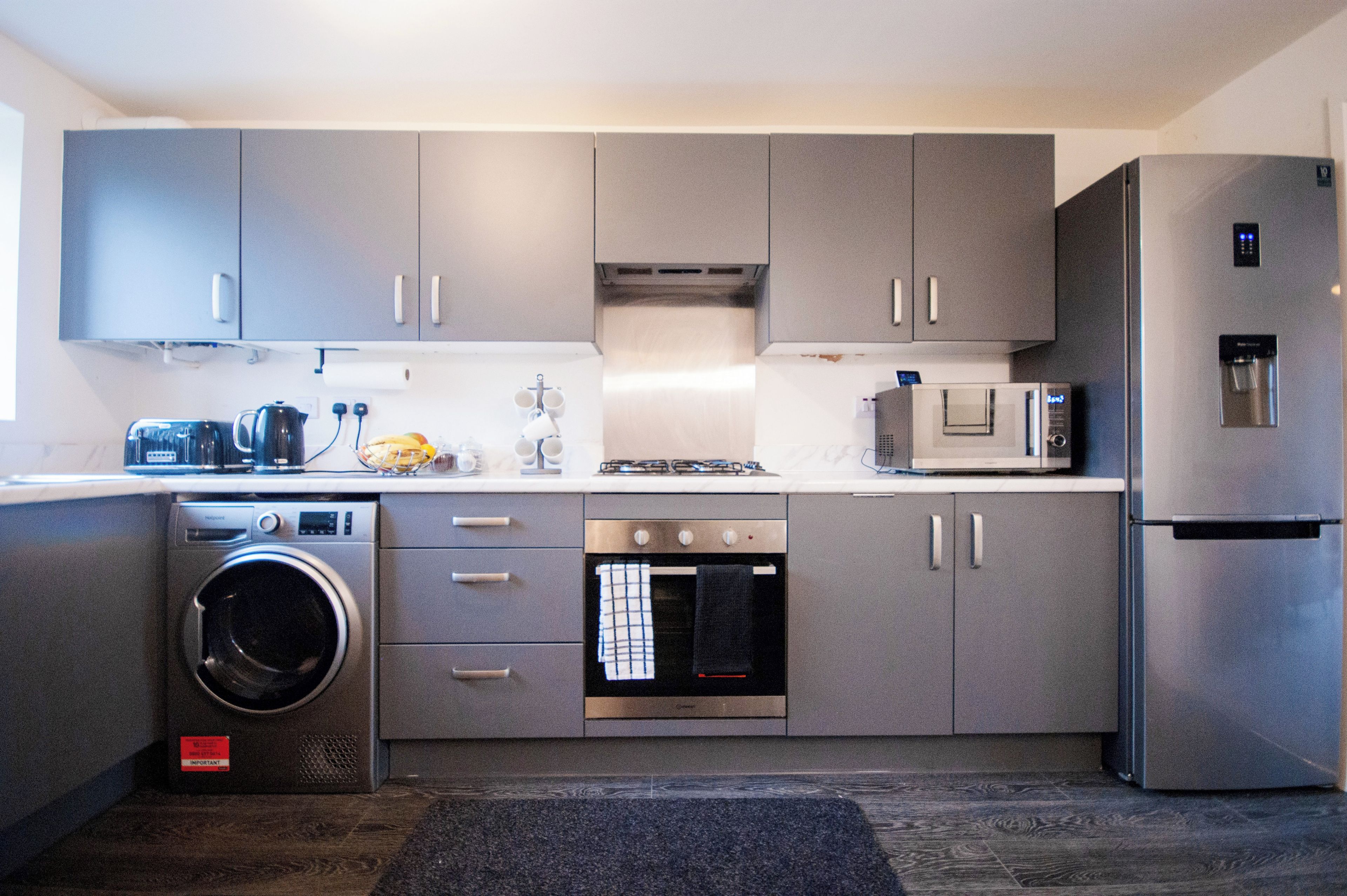 A compact kitchen with grey cabinets, a built-in washing machine, a microwave, and a refrigerator.