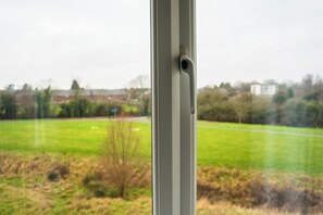 A window with a view of a green field and a building in the distance. - Cozy Coventry Retreat - 3 Bedroom House (Coventry)
