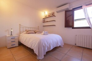 A bedroom with a bed, bedside table, wall-mounted shelves, and a window with curtains. - Classic Ibiza Villa · Pool + Garden + 3 Bedrooms (Islas Baleares)