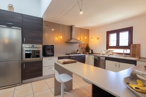 A modern kitchen with a built-in oven, a microwave, a stovetop, and a dishwasher. There is a large island with a cutting board and a banana on a wooden bowl. - Classic Ibiza Villa · Pool + Garden + 3 Bedrooms (Islas Baleares)