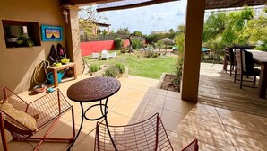 An outdoor patio area with a covered seating area, a table, and a dog crate. - Classic Ibiza Villa · Pool + Garden + 3 Bedrooms (Balearic Islands)