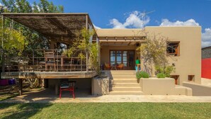 A modern house with a covered outdoor seating area, a staircase leading to the entrance, and a well-maintained lawn. - Classic Ibiza Villa · Pool + Garden + 3 Bedrooms (Balearic Islands)