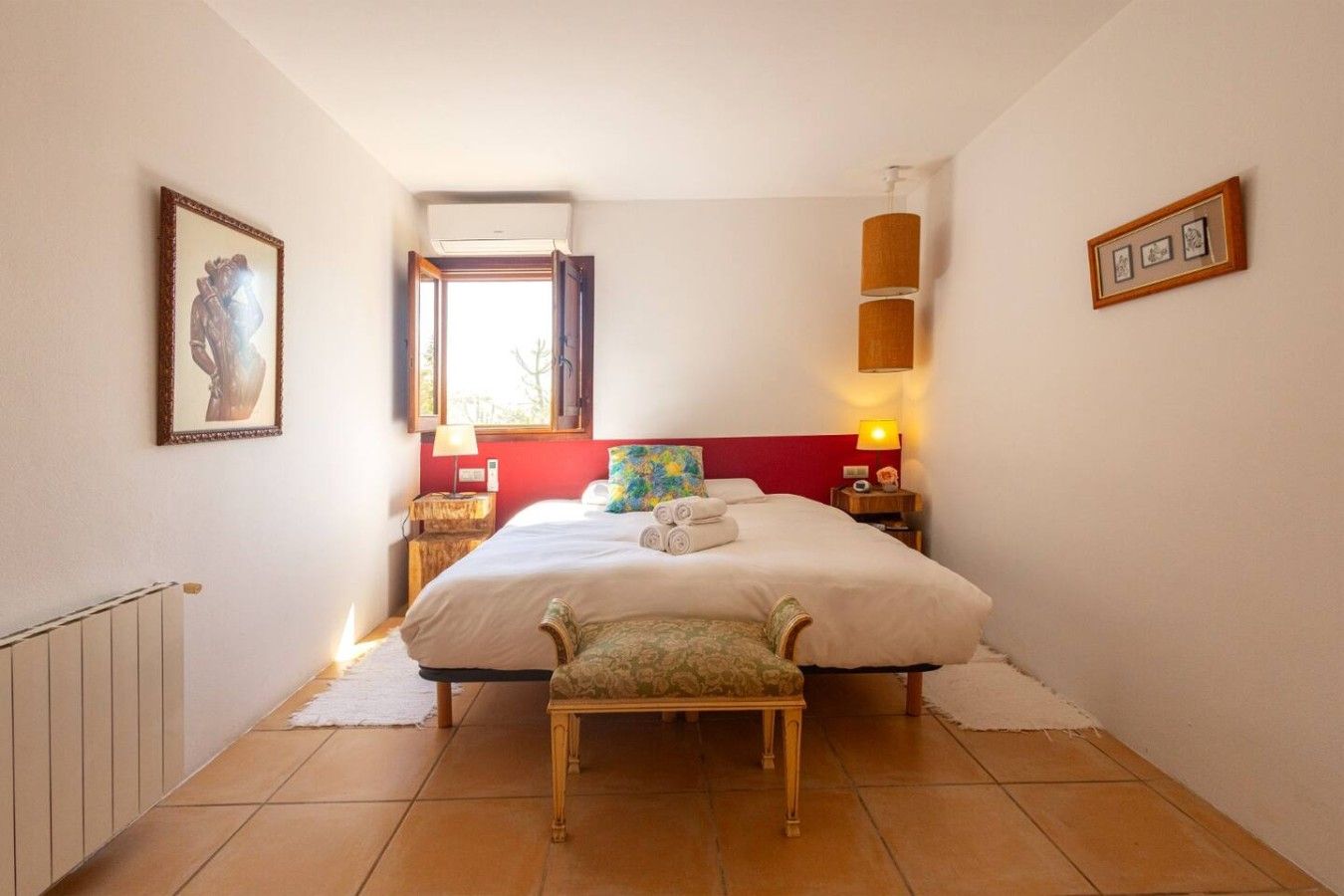Een hotelkamer met een bed, een bankje, een raam, een wandairconditioner en een lamp.