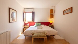 A hotel room with a bed, a bench, a window, a wall-mounted air conditioner, and a lamp. - Classic Ibiza Villa · Pool + Garden + 3 Bedrooms (Balearic Islands)