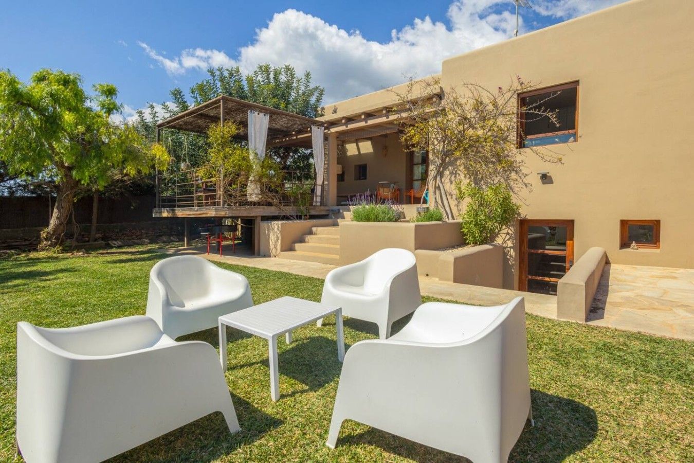 A modern outdoor seating area with white chairs and a table, a covered patio, and a building with a flat roof and large windows.