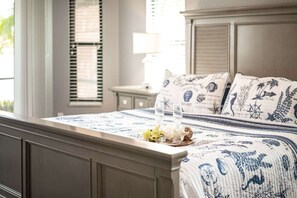 A neatly made bed with a blue and white patterned bedspread, two clear glasses on a tray, and a nightstand with a lamp. - Villa Glasswater - Lake View, Kajaks & Dock (Cape Coral)