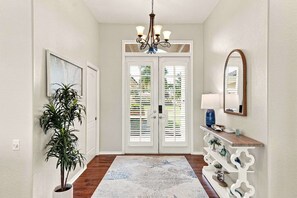 A hallway with a chandelier, a potted plant, a console table with a mirror, and a patterned rug. - Villa Glasswater - Lake View, Kajaks & Dock (Cape Coral)