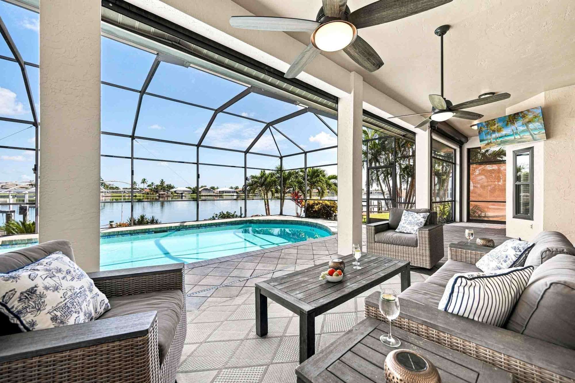 Un área junto a la piscina con una piscina cubierta con vidrio, mobiliario exterior y ventiladores de techo.