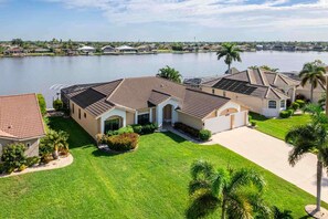 A residential area with houses near a body of water, featuring well-maintained lawns and palm trees. - Villa Glasswater - Lake View, Kajaks & Dock (Cape Coral)