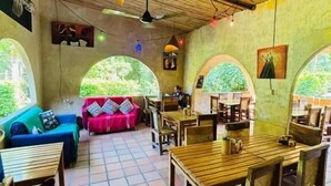 Habitació amb sòl de rajola, mobles de fusta i sostre de palla. Hi ha finestres que donen vistes a vegetació.