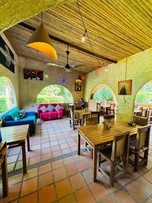 A room with a tiled floor, wooden furniture, and a thatched ceiling. There are windows with views of greenery. - Finca Carpe Diem ecoodge (Minca)
