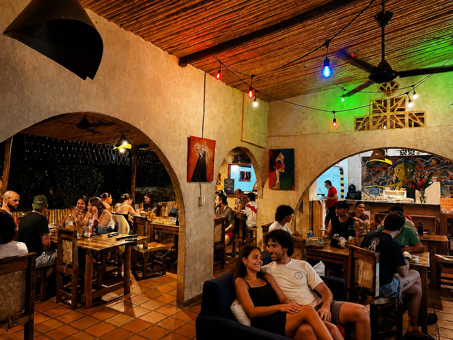 Un comedor interior con mesas y sillas de madera, una zona de bar y obras de arte en las paredes.