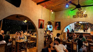 Un comedor interior con mesas y sillas de madera, una zona de bar y obras de arte en las paredes.