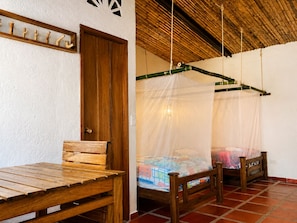 Una habitación con un banco de madera, una cama con mosquitero y una puerta de madera.