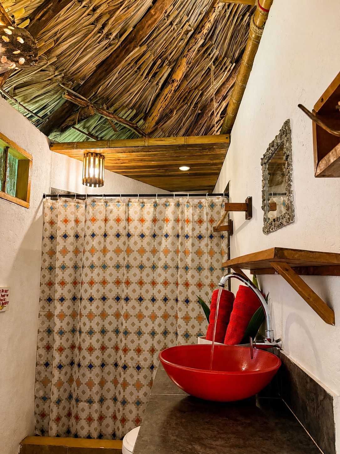 Un baño con cortina de ducha, un lavabo rojo y techo de madera.