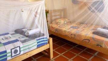 Dos camas de madera con mosquiteros, una con almohada a rayas y otra con almohada estampada, sobre un piso de baldosas.